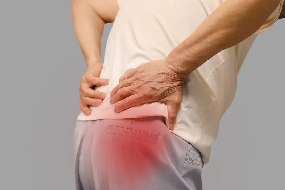 Person holding their lower back with a red pain indicator radiating down the hip — a common presentation of herniated disc symptoms treated in Morganville, NJ.