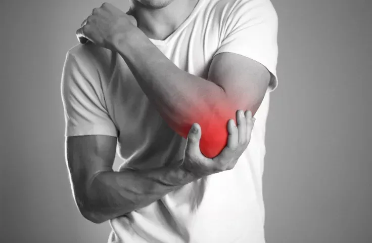 A man holds his elbow with a pained expression, highlighted to indicate the area of discomfort. Limitless Spine & Joint Care offers integrated elbow-pain treatment in Morganville, NJ.