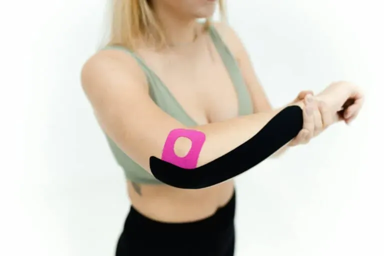 A person with kinesiology tape applied to their arm to alleviate elbow pain. The tape is black and pink, applied by Limitless Healthcare Team.