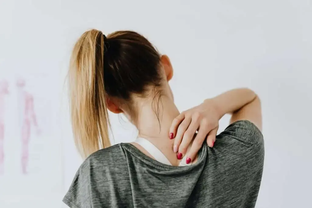 A woman faces away from the camera, holding the back of her neck with a pained expression. Limitless Spine & Joint Care offers integrated neck-pain treatment in Morganville, NJ.