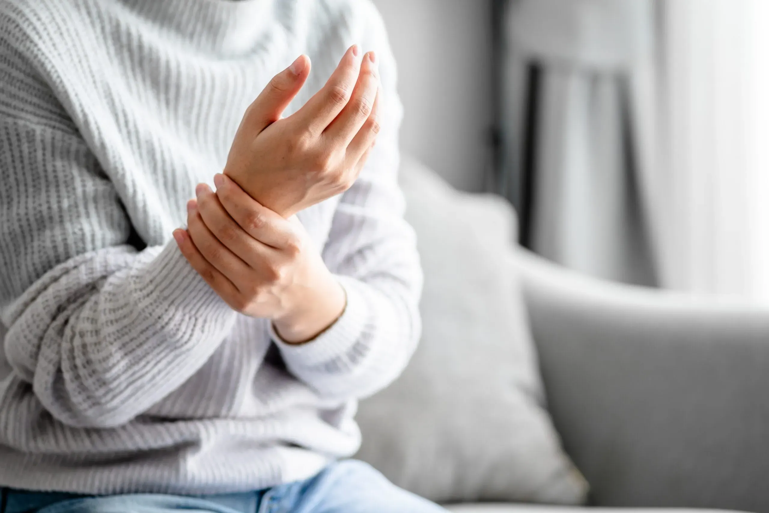 A person in a light sweater cradling their wrist in visible discomfort — depicting numbness, tingling, and nerve pain symptoms evaluated at Limitless Spine & Joint Care in Morganville, NJ.