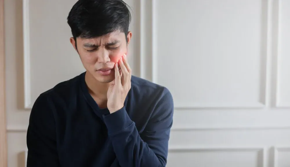 A young man in close-up frowns and holds his hand to his jaw, indicating TMJ pain. Limitless Spine & Joint Care offers integrated TMJ-disorder treatment in Morganville, NJ.